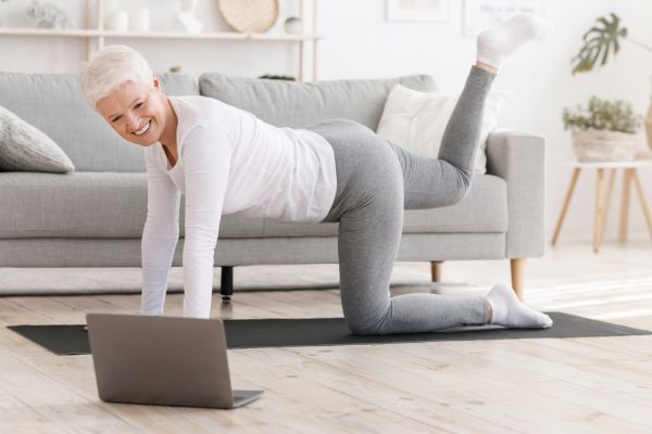 Eine Frau macht Rückenübungen auf dem Boden vor einem Laptop.